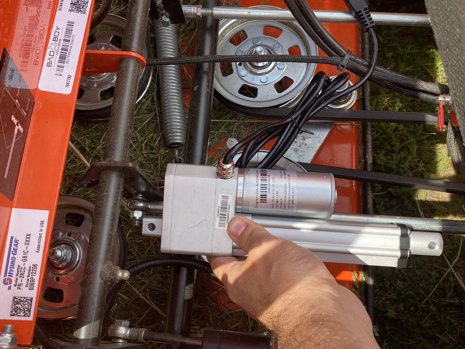 PA-01-4-56-POT-12VDC linear actuator in hand against the Bad Boy frame on arrival day, 2026-05-08